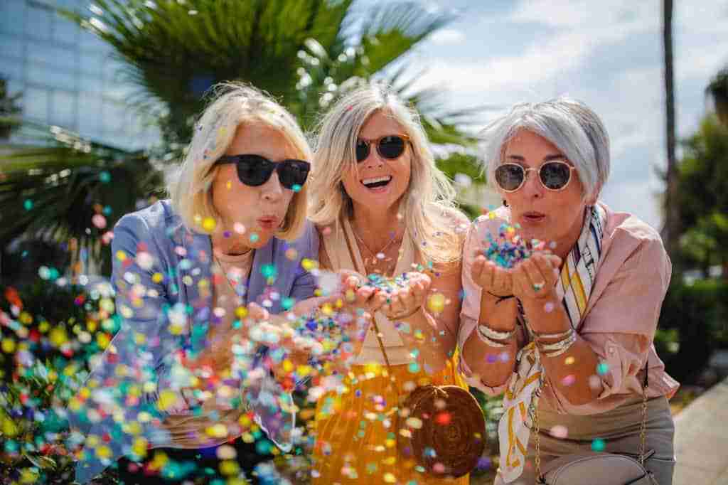 Fashionable mature friends having fun and celebrating by blowing colorful confetti in city street